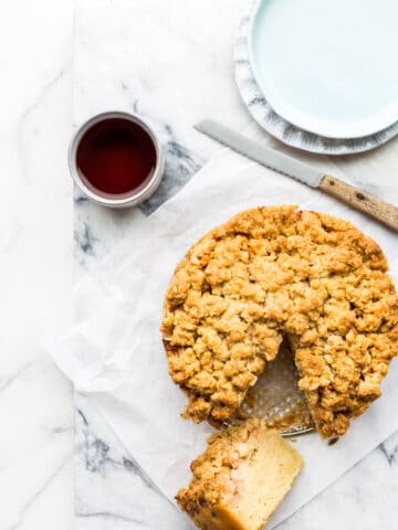 Apple crumb coffee cake ready to be served with cups of tea, plates and a serrated knife