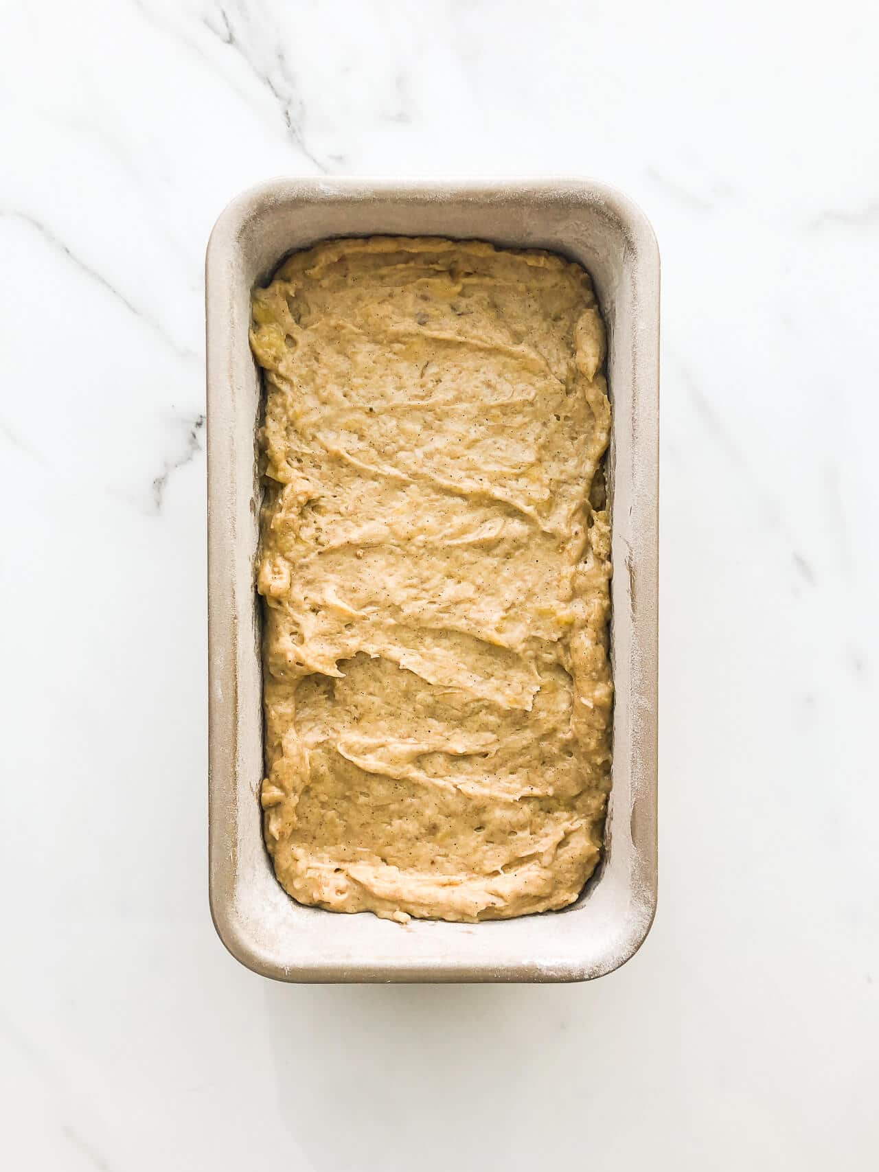 Banana bread batter in a loaf cake pan on marble surface