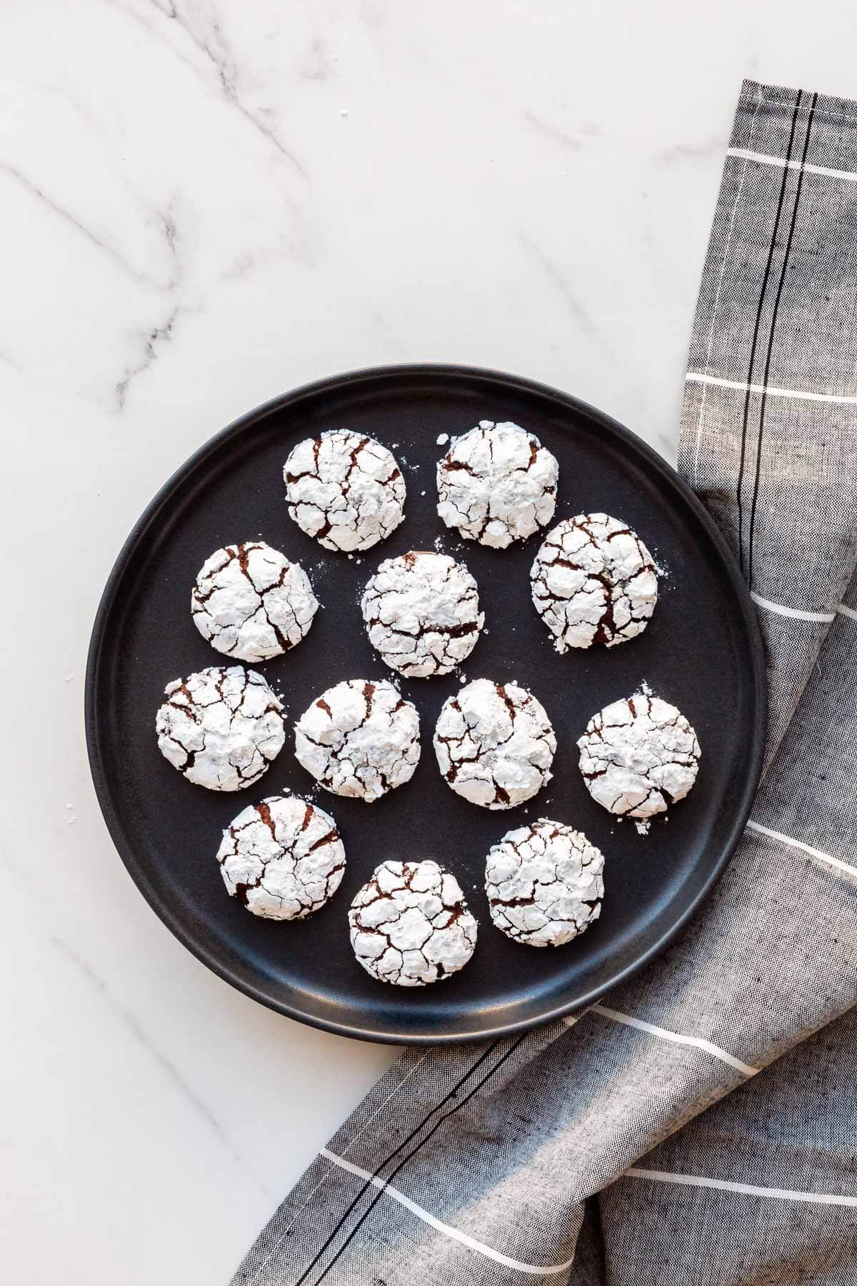 A black plate with chocolate crinkle cookies on it.
