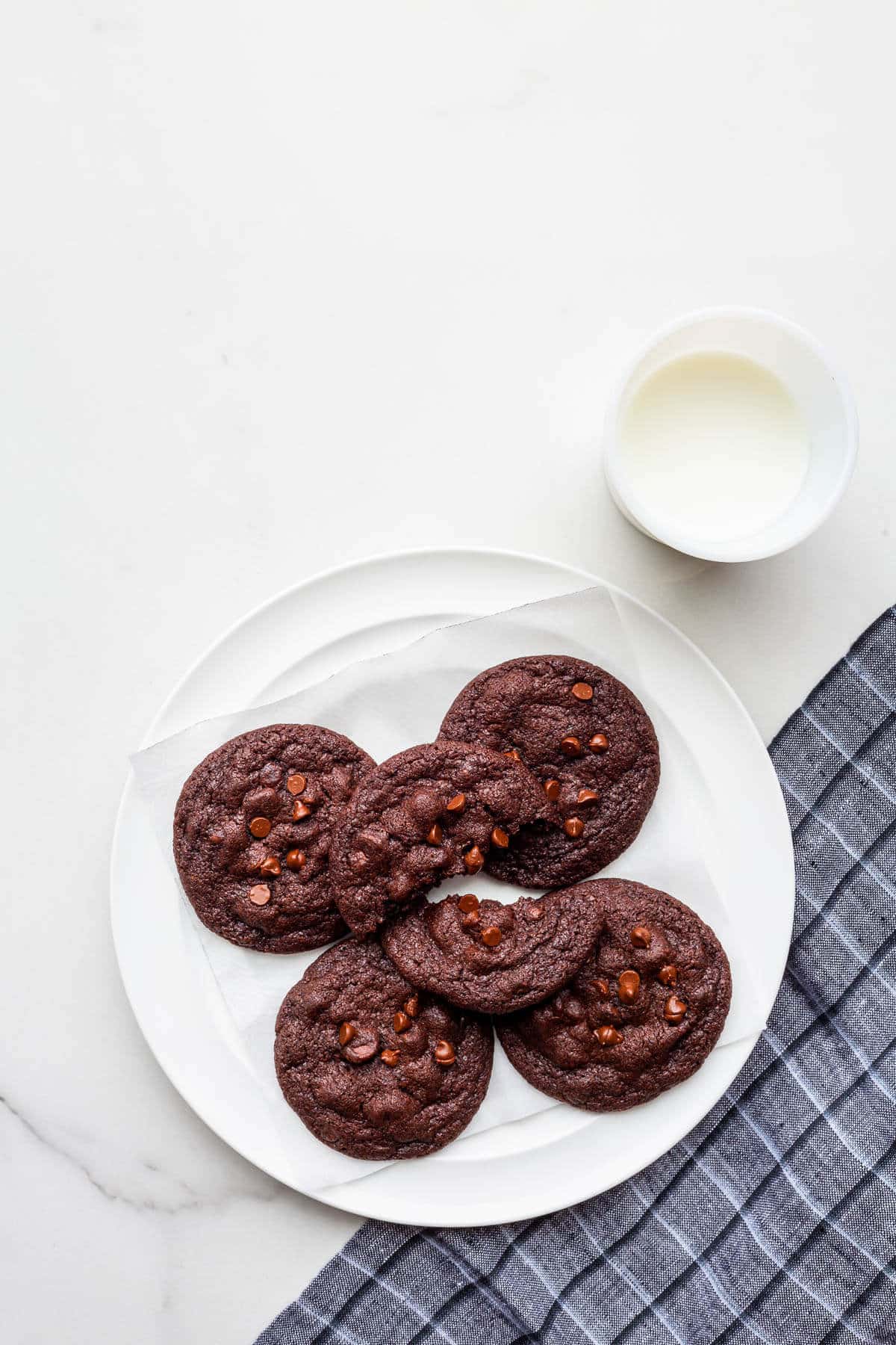 A plate of double chocolate chip cookies with a glass of milk.