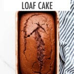 Baked chocolate loaf cake in loaf pan with striped linen tucked underneath.