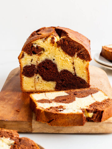 Slicing a chocolate and vanilla marble cake on a cutting board.