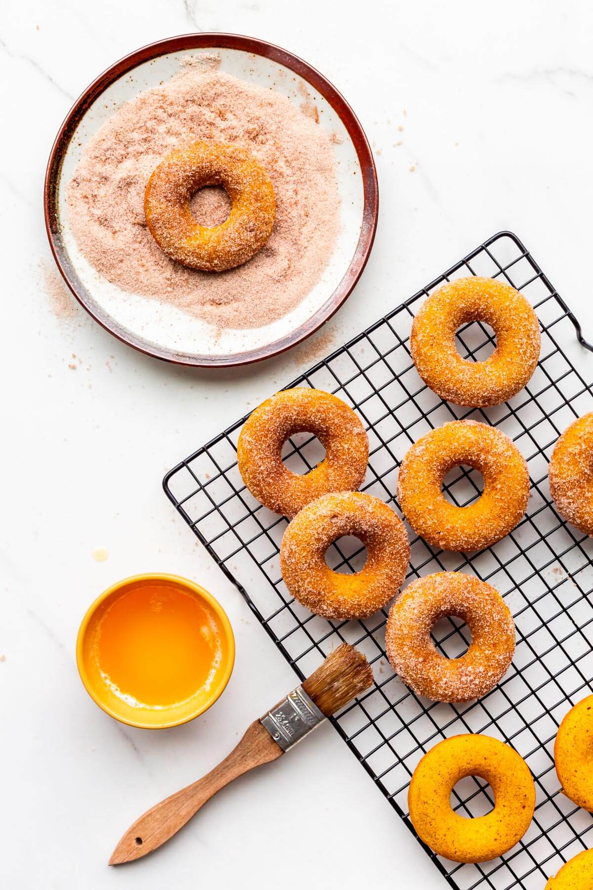 Brushing baked pumpkin donuts with melted butter and coating in cinnamon sugar before eating.