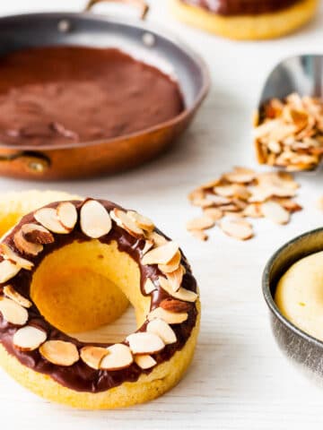 Baked donuts dipped in chocolate icing and topped with sliced almonds.