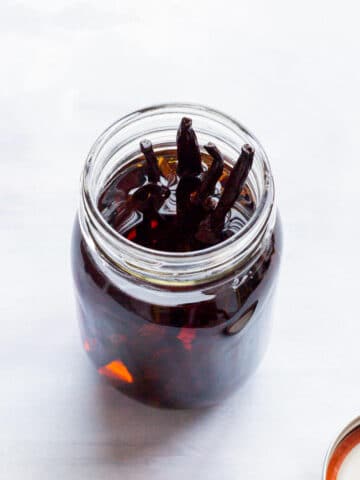 An open jar of homemade vanilla extract with vanilla beans poking up above the alcohol.