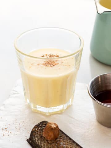A small glass of eggnog topped with freshly grated nutmeg and a shot of rum to mix into it.