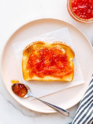 Pink grapefruit marmalade on toast on a plate with a striped linen.