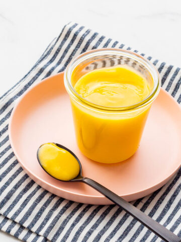 A jar of lemon curd set on a pink plate.
