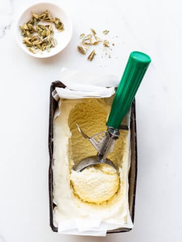 Scooping homemade cardamom ice cream with a disher. Small bowl of cardamom pods nearby