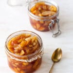Two jars of spiced apple jam made with chunks of apple and served with a teaspoon