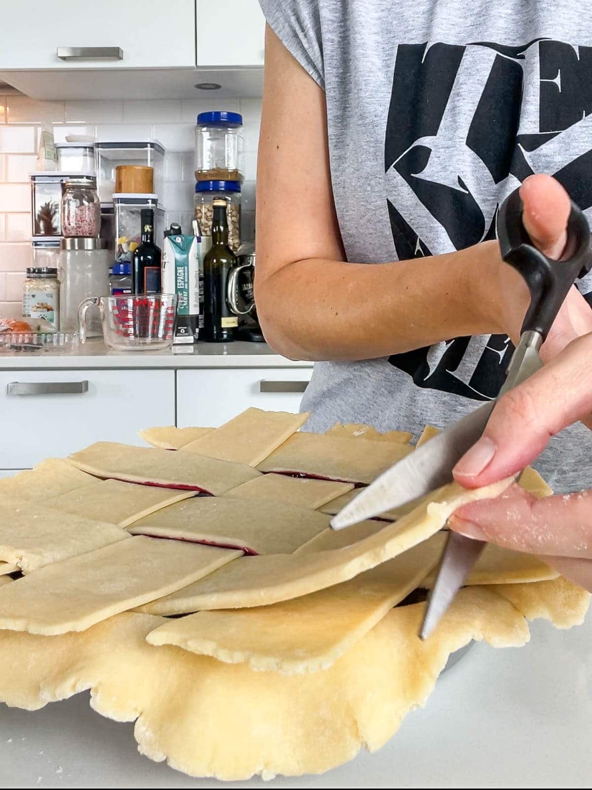 Cutting excess dough from a lattice pie crust with kitchen scissors to ensure the crust edges aren't too thick.