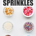 Different types of colourful sprinkles, quins, and sanding sugar in small bowls.