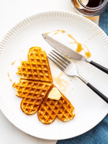 Waffles on a plate with maple syrup and a pat of butter.